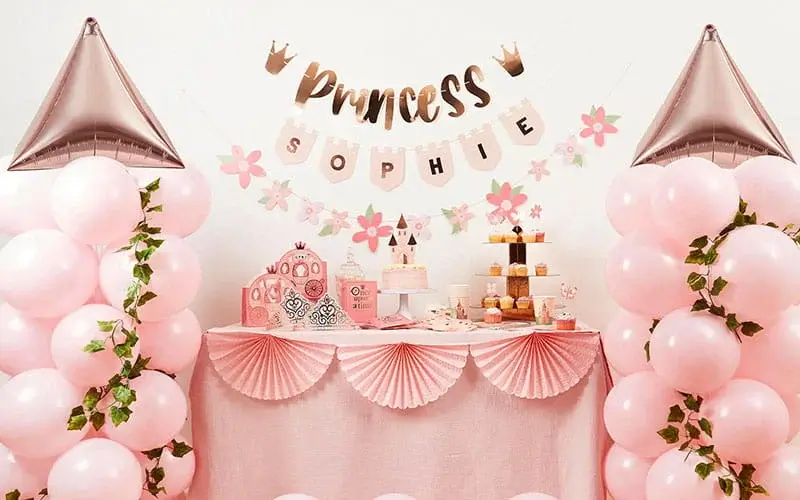 Princess-themed party display with pink balloons, a dessert table, castle decorations, cupcakes, and a personalised princess birthday banner.